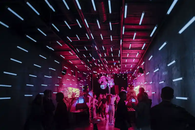 [Interior oscuro de un bar de copas con luces de neón y copas de colores listas en la barra]